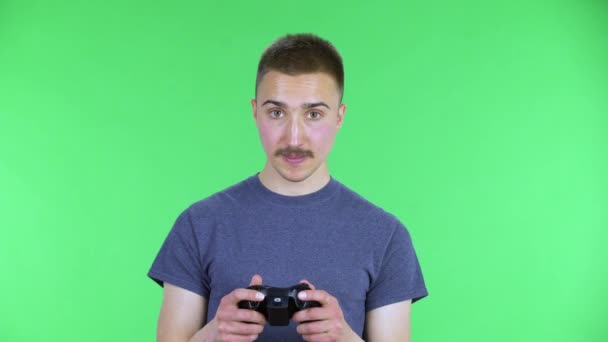 Portret młodego człowieka grającego w grę wideo, korzystającego z bezprzewodowego kontrolera, cieszącego się zwycięstwem i przegrywającego. Słodki mężczyzna z wąsami, pozujący na zielonym ekranie w studiu. Zamknij się.. — Wideo stockowe