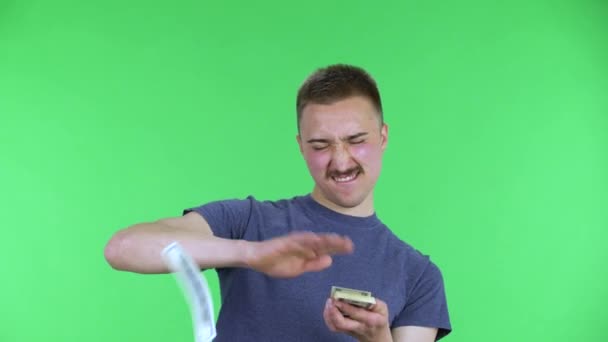 Portrait of a young man is rejoices and scatters money. Cute male with a mustache in a blue t-shirt posing on a green screen in the studio. Close up. — Stock Video