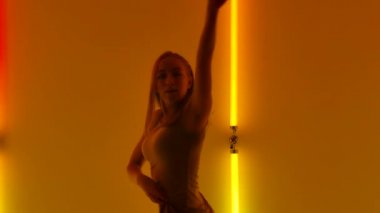 Kadın dansçı, çağdaş küçümseme koreografisinin duygusal dans unsurlarını icra eder. Nazik genç bayan karanlık stüdyoda neon ışıklarının arka planında zarif bir şekilde dans ediyor. Kapatın. Yavaş çekim.