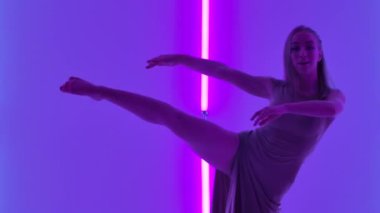 Kadın dansçı şehvetli bir küçümseme sergiliyor ve zarif bir şekilde parlak neon ışıkların arkasına zıplıyor. Karanlık bir stüdyoda modern koreografiyle dans eden genç bir kadın. Kapatın. Yavaş çekim.