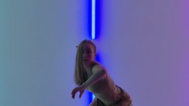 Bej elbiseli modern bayan dansçı karanlık stüdyoda güzel plastik dramatik danslar yapıyor. Esnek dans eden kadın parlak renkli neon ışıkların arka planına karşı. Kapatın. Yavaş çekim.