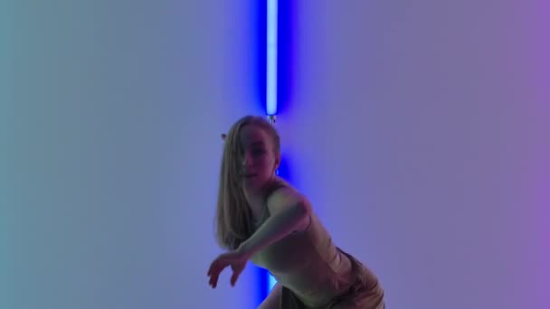 穿着米色衣服的现代女舞蹈演员在黑暗的演播室里表演美丽的塑料舞曲。柔韧的女人在明亮的霓虹灯的映衬下跳舞。靠近点慢动作. — 图库视频影像