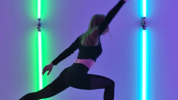 Young dancer demonstrates sensual movements by dancing contemp against backdrop of bright neon lights. Athletic woman performing emotional modern choreography in twilight studio. Close up. Slow motion — стоковое видео