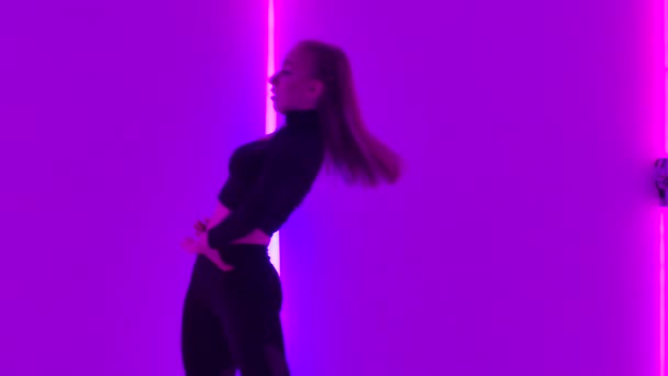 Flexibel dansare utför akrobatiska inslag av modern koreografi och hoppar mot en bakgrund av lila neonljus. Sensuell kvinna utövar förakt i skymningsstudio. Närbild. Långsamma rörelser. — Stockvideo