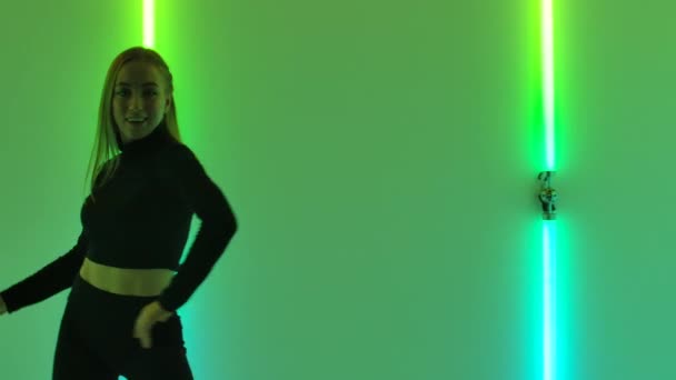 Ballerino professionista gira e salta, elementi di danza disprezzo in uno studio buio su uno sfondo di luci al neon verde brillante. Una donna snella dimostra flessibilità del corpo al rallentatore. Da vicino.. — Video Stock