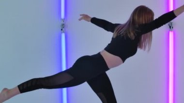 İnce dansçı tarafından icra edilen aerobik elementlerle, parlak neon ışıkların arka planına karşı duygulu ve modern bir aşağılama. Kadın, karanlık stüdyoda modern koreografi uyguluyor. Kapatın. Yavaş çekim.