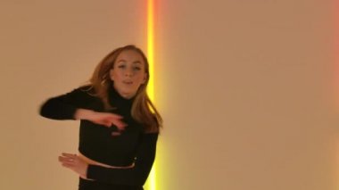 Profesyonel dansçı tarafından yapılan nazikçe çağdaş küçümseme koreografisi sarı neon ışıkların arka planına karşı. İnce kadın, akrobasi öğeleriyle aşağılayıcı bir şekilde dans ediyor. Kapatın. Yavaş çekim.