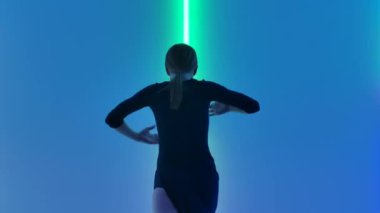 Zayıf dansçı tarafından icra edilen akrobatik öğelere nazik bir aşağılama. Modern koreografiden hoşlanan genç ve güzel bir kadın karanlık stüdyoda parlak neon ışıkların önünde. Kapatın. Yavaş çekim.
