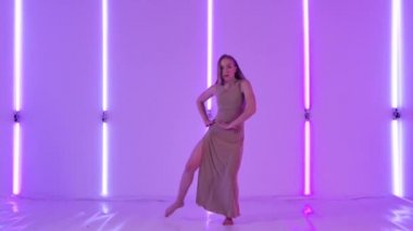 Kadın dansçı şehvetli bir küçümseme sergiliyor ve zarif bir şekilde parlak neon ışıkların arkasına zıplıyor. Karanlık bir stüdyoda modern koreografiyle dans eden genç bir kadın. Yavaş çekim.