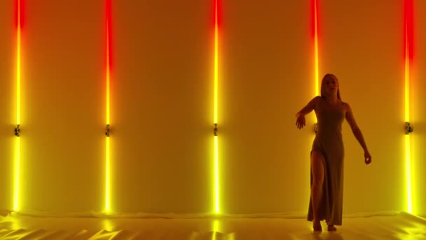 Femela dansatoare interpretează elemente de dans emoțional ale coregrafiei contemporane de dispreț. O tânără blândă dansează grațios într-un studio întunecat pe fundalul luminilor de neon roșu galben. Slow motion . — Videoclip de stoc