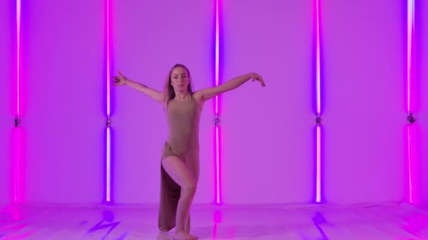 Feminin kvinnlig dansare utför sensuellt förakt och hoppar graciöst mot bakgrund av starkt neonljus. Ung kvinna dansar modern koreografi i en mörk studio. Långsamma rörelser. — Stockvideo