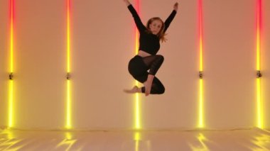 Profesyonel dansçı tarafından yapılan nazikçe çağdaş küçümseme koreografisi sarı neon ışıkların arka planına karşı. İnce kadın, akrobasi öğeleriyle aşağılayıcı bir şekilde dans ediyor. Yavaş çekim.