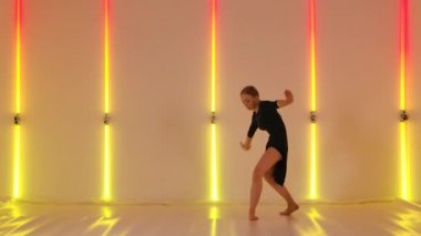 Çekici dansçı, kırmızı sarı neon ışıklara karşı modern bir aşağılama koreografisi sergiliyor. Genç kadın akrobasi öğeleriyle dans ediyor. Yavaş çekim.