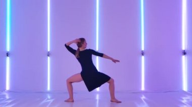 Tatlı, genç bir kadın zarif bir şekilde neon ışıkların arka planına karşı şehvetli bir küçümsemeyle zıplar ve döner. Siyah elbiseli ince dansçı yavaş çekimde esnekliğini gösteriyor..