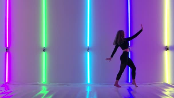 Genç dansçı, parlak neon ışıklarının arka planında dans ederek şehvetli hareketler sergiliyor. Alacakaranlık Stüdyosunda duygusal modern koreografi sergileyen atletik bir kadın. Yavaş çekim. — Stok video