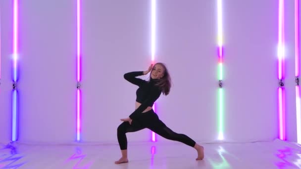 Dansator fermecător în tricou negru care efectuează elemente acrobatice de dans contemp pe fundalul luminilor luminoase de neon. Flexibil sexy femeie se mișcă în mișcare lentă . — Videoclip de stoc