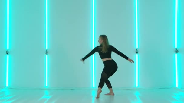 Charmante Tänzerin im schwarzen Trikot, die vor dem Hintergrund greller Neonlichter akrobatische Wettkampftanz-Elemente vorführt. Flexible sexy Frau bewegt sich in Zeitlupe. — Stockvideo