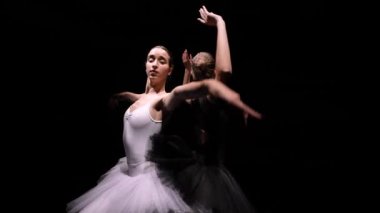 Kamera, siyah beyaz etekli iki esnek balerin etrafında döner ve ellerini arka plandaki siyah stüdyoya doğru çarpıcı bir şekilde hareket ettirir. Yörünge atışı. Kapatın. Yavaş çekim.