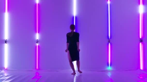 Delicato disprezzo per gli elementi acrobatici eseguiti dalla sottile ballerina in abito nero. Bella giovane donna godendo coreografia moderna su uno sfondo di luci al neon luminose in studio buio. Rallentatore. — Video Stock