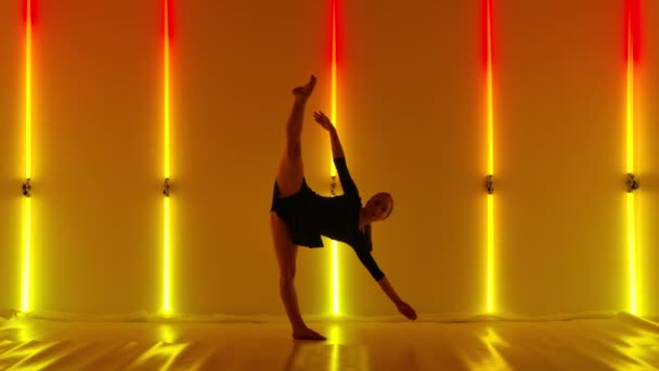 Attractive dancer emotionally performs modern choreography of contempt against backdrop of red yellow neon lights. Young woman is dancing contemp with elements of acrobatics. Slow motion. — стоковое видео