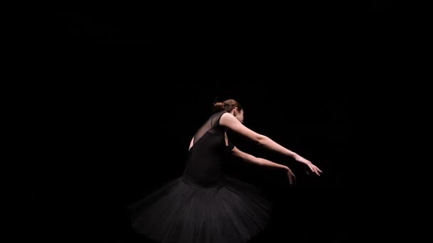 Captura orbital de una bailarina en la imagen de un cisne negro que se mueve elegantemente sobre un fondo de estudio negro con luz de fondo. De cerca. Movimiento lento. — Vídeo de stock