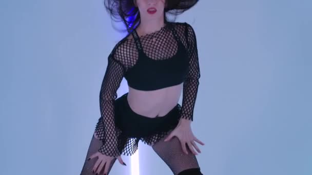 Sexy danser voert een erotische strip dans in donkere studio tegen de achtergrond van heldere neon lichten. De benige brunette op hoge hakken demonstreert de flexibiliteit van de figuur. Sluit maar af. Langzame beweging — Stockvideo