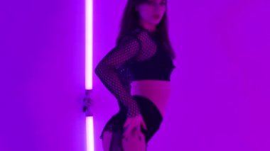 Muhteşem vücutlu seksi esmer, karanlık stüdyoda parlak neon ışıkların önünde erotik danslar yapıyor. Striptizci cinselliğini ve esnekliğini gösteriyor. Kapatın. Yavaş çekim.