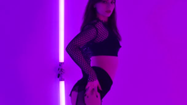 Hot brunette met prachtige lichaam erotisch danst strip in donkere studio tegen de achtergrond van heldere neon lichten. Stripper toont haar seksualiteit en flexibiliteit. Sluit maar af. Langzame beweging. — Stockvideo
