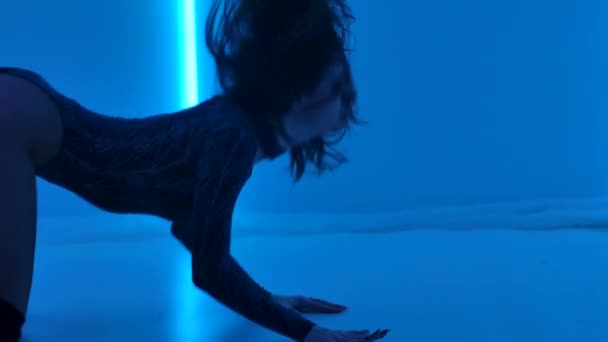 연성 브라 무네 는 밝은 네온등을 배경으로 어두운 스튜디오 에서 춤추는 것을 좋아한다. 멋진 몸에 끈을 두르고 성적으로 다리를 벌리고 바닥에서 뒹굴고 있다. 닫아. 느린 동작. — 비디오