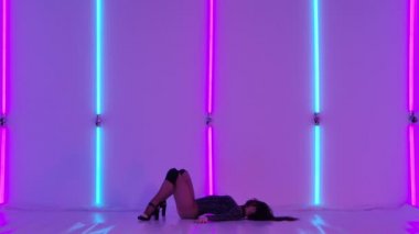 Ateşli bir esmer, erotik bir şekilde vücuduna dokunur ve bacaklarını geniş aralıklarla açar ve çıplak plastik elementler sergiler. Dar siyah elbiseli ve topuklu ayakkabılı baştan çıkarıcı striptizci. Yavaş çekim.