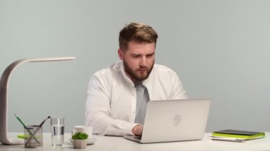 Genç iş adamı dikkatle düşünüyor ve klavyede daktilo kullanıyor. Freelancer merkez ofiste otururken uzaktan çalışıyor. İnterneti kullanarak kişisel izolasyon sırasında çevrimiçi çalışma. Kapatın. Yavaş çekim.