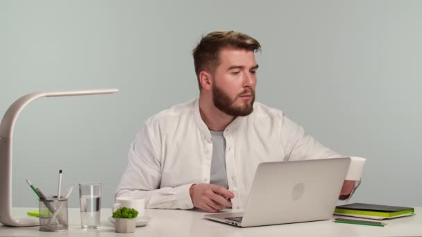 年轻的自由职业工人用酒精消毒剂喷雾和餐巾纸给笔记本电脑消毒。男性坐在总公司的餐桌前。在线学习或自我隔离期间的远程工作。靠近点慢动作. — 图库视频影像