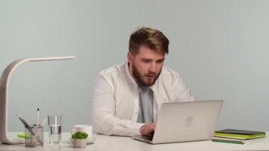 Genç başarılı serbest çalışan evde oturmuş bilgisayarında gülümsüyor ve daktilo yazıyor. Yakışıklı bir adam başarıya sevinir. Uzaktan çalışma konsepti, online öğrenme. Kapatın. Yavaş çekim.