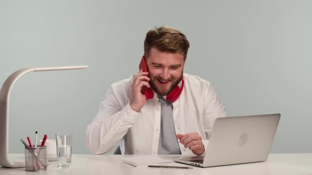 家のオフィスに座っている間、積極的な髭の男はノートパソコンでリモートで働いています。フリーランスは仕事を中断し、フレンドリーな電話を持っています。家庭から働くという新しい概念。閉めろ。スローモーション. — ストック動画