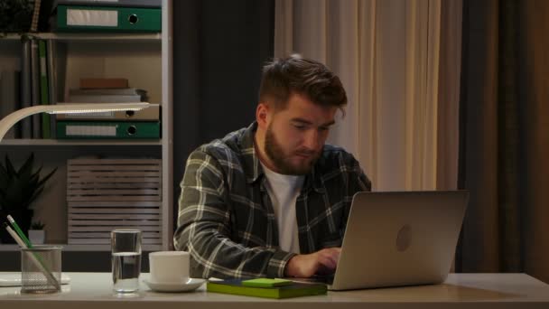 Vermoeide jongeman werkt aan laptop wrijven uw tempels en squinting op kantoor. Uitgeputte jonge freelancer lijdt aan migraine overwerkt op de computer. Sluit maar af. Langzame beweging. — Stockvideo