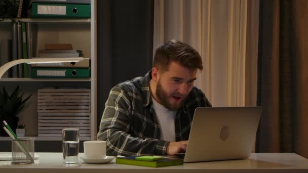 Mannelijke freelancer heeft videogesprekken met een klant, kijkt naar een laptopscherm en bespreekt een nieuw opstartproject terwijl hij vanuit zijn kantoor thuis werkt. Verheugt zich over een succesvolle deal. Sluit maar af. Langzame beweging. — Stockvideo