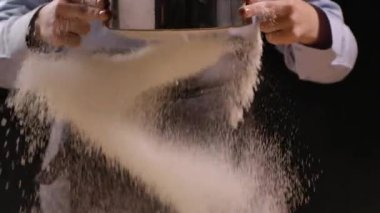 Kadın şef, süzgeçten doğal buğday unu geçirir. Beyaz toz masaya ağır çekimde düşer. Hamur hazırlama süreci. Kapat..