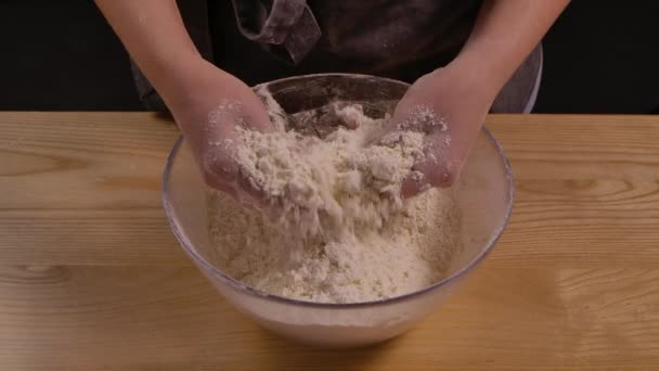 A lisztből kézzel készített tészta készítésének folyamata. A pék női kezek fehér lisztet öntenek egy üvegtálba, és összekeverik. Lépcsők főzés és cukrászda. Bezárás, lassított felvétel.. — Stock videók