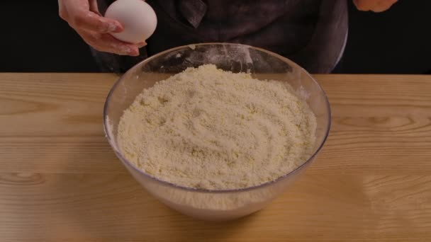 A női kéz eltöri a tojást, hogy elkészítse a hagyományos tésztát. Tojás esik üvegtálba elkészített liszt és tészta összetevőket. A lisztből kézzel készített tészta készítésének folyamata. Bezárás, lassított felvétel.. — Stock videók