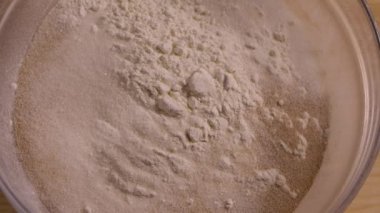 Tereyağının üst görüntüsü, mutfakta ahşap masada duran unlu cam kaseye düşer. Undan el yapımı hamur yapma süreci. Pişirme ve şekerleme pişirme adımları. Yaklaşın, ağır çekim.