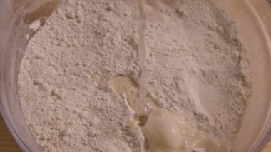 Hamur yoğurmak için malzemelerle dolu cam bir kasenin üst görüntüsü. Un, şeker, tereyağı ve maya üzerine su dökülür. Undan el yapımı hamur yapma süreci. Yaklaşın, ağır çekim..