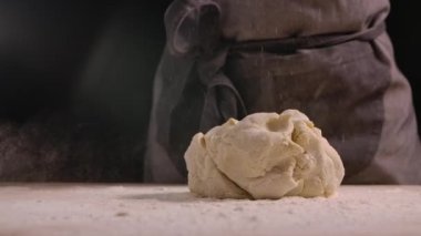 Hamur un kaplı mutfak masasına düşer. Beyaz un farklı yönlere dağılır. Undan el yapımı hamur yapma süreci. Pişirme ve şekerleme pişirme adımları. Yaklaşın, ağır çekim.