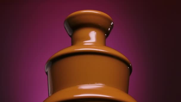 Płynna czekoladowa fontanna do słodkich deserów fondue, widok z niskiego kąta. Słodki stopiony deser przepływa przez kaskadę czekoladowej fontanny na fioletowym tle. Zamknij drzwi. Zwolniony ruch. — Wideo stockowe