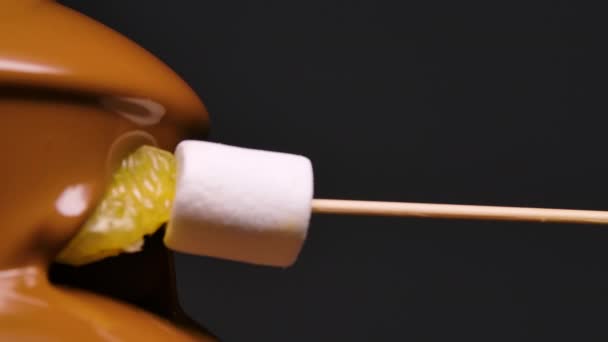 Melted milk chocolate flows in chocolate fountain. Marshmallows and orange slice on skewer are dipped in sweet melted chocolate. Fondue. Gourmet food. Party and celebration. Close up. Slow motion. — Stock Video