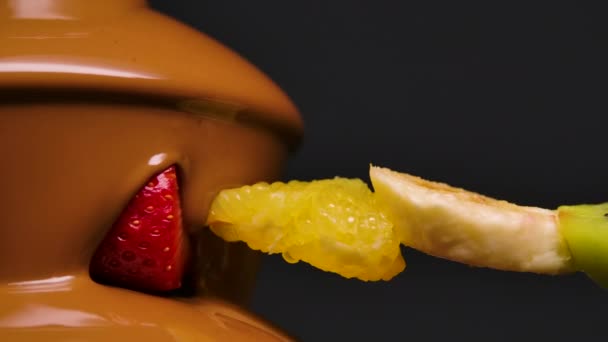 Melted milk chocolate flows in chocolate fountain. Ripe juicy fruits on skewer are dipped in sweet melted chocolate. Fondue. Dessert. Gourmet food. Party and celebration. Close up. Slow motion. — Stock Video