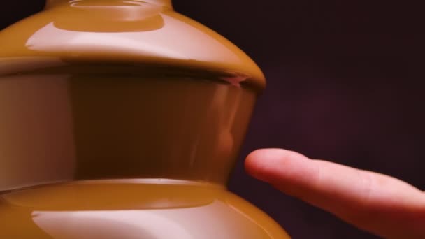 Chocolate de leite derretido flui em uma fonte de chocolate. Um homem mergulha o dedo em chocolate líquido quente. Fondue. Festa e celebração. Fecha. Movimento lento. — Vídeo de Stock