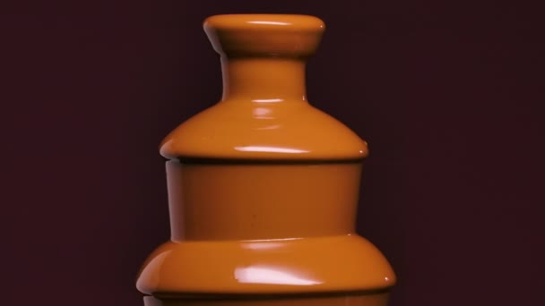 The opening of the chocolate fountain. A stream of molten hot chocolate flows out of the tower and cascades down. Drops of sweet thick dessert on dark purple background. Close up. Slow motion. — Stock Video