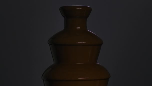 Chocolate fountain. Liquid chocolate flows down a cascade against a light purple background. Hot chocolate dessert in bright light and dark. Sweet food. Celebration decoration. Close up. Slow motion. — Stock Video