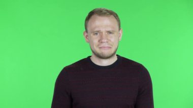 Orta yaşlı bir adamın portresi. Heyecanlı, alıngan ve çok üzgün. Siyah kırmızı kazaklı traşsız bir erkek stüdyoda yeşil ekranda poz veriyor. Kapat..