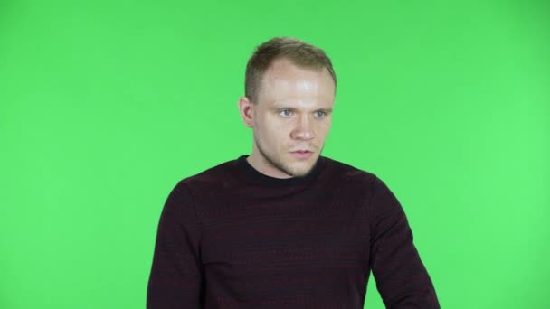 Porträt eines Mannes mittleren Alters steht nervös in Erwartung, blickt sich um, ist wütend. Unrasierter Mann im schwarz-roten Pullover posiert auf einer grünen Leinwand im Studio. Nahaufnahme.